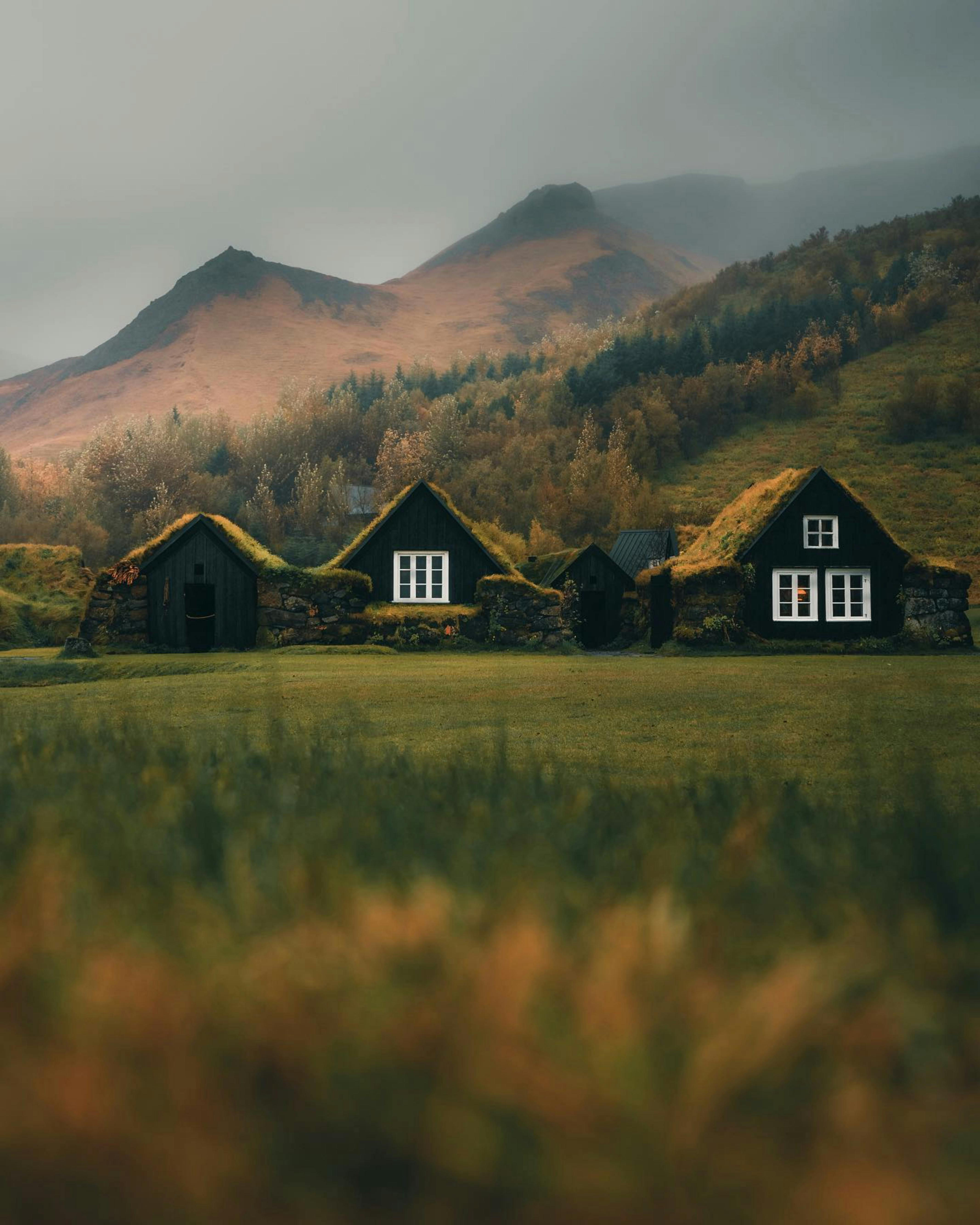 Charming turf houses nestled in the misty Icelandic mountains, offering a serene view.