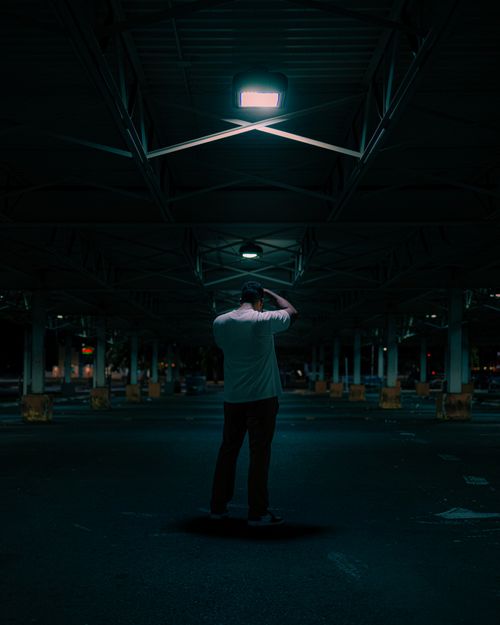 Free A lone man stands under a light in an empty urban parking garage at night. Stock Photo