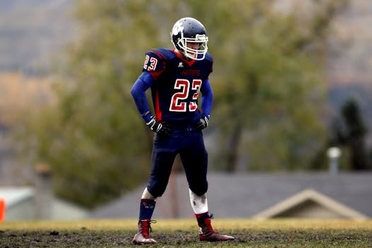 Athlete in full gear standing on football field, helmet and uniform visible.