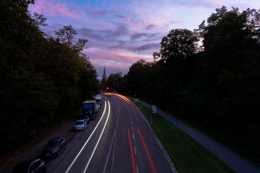 Street scene in Karlsruhe at dusk with car light trails and colorful sky.