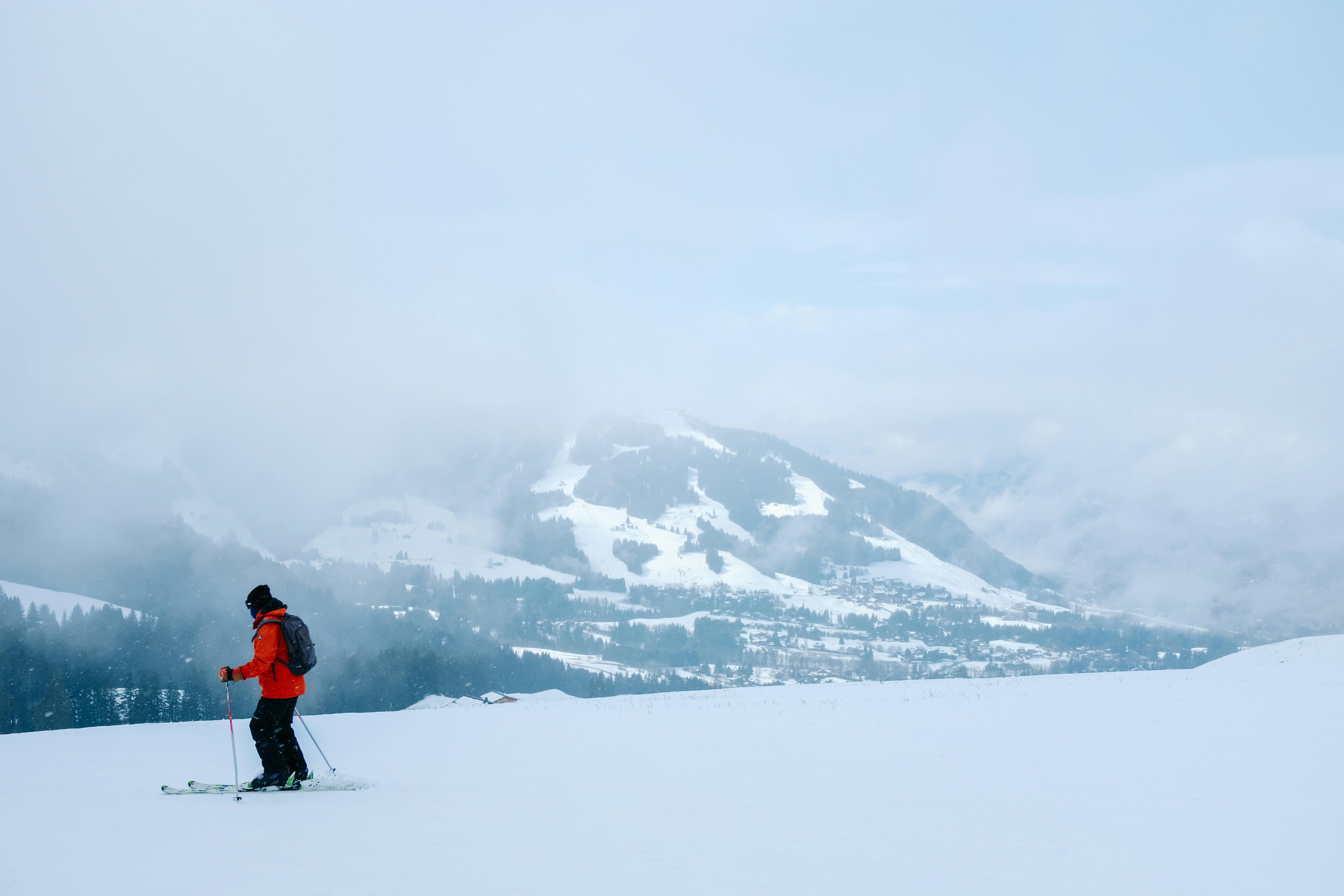 A skier in red navigates a snow-covered mountain slope with foggy hills in the background.