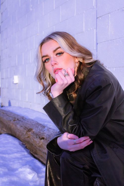 Free Stylish woman poses in a black leather coat against a white wall, capturing winter fashion on a city street. Stock Photo