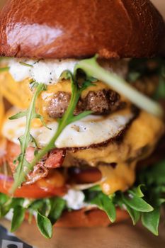 Close-up of a gourmet beef burger layered with arugula, cheese, and an egg, showcasing delicious ingredients.