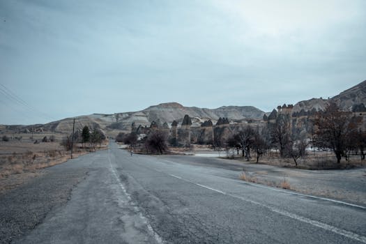 Empty highway stretching through unique rock formations and arid landscape under a broad sky.