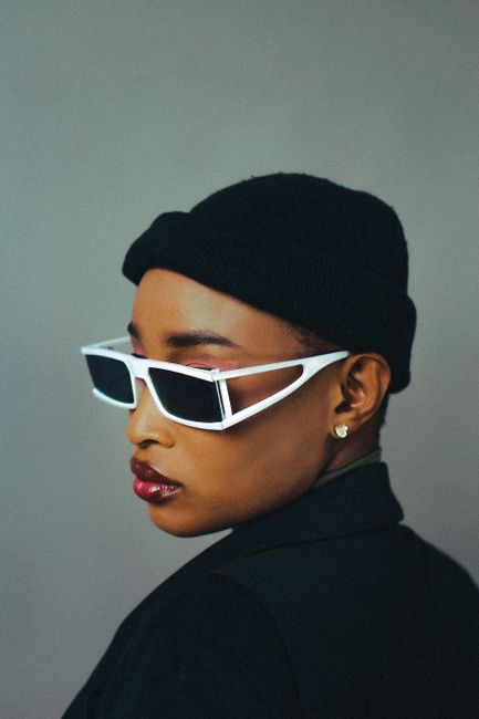 Stylish portrait of a woman wearing sunglasses and a hat against a grey background.