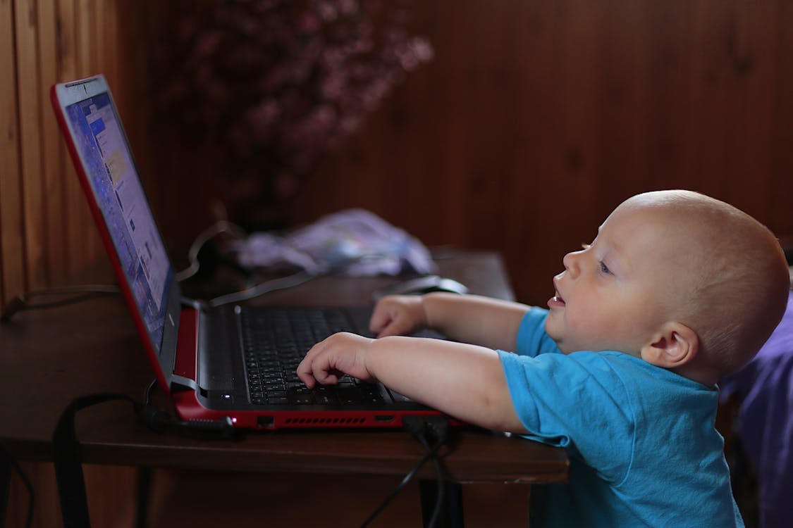 Ragazzo Che Indossa La Maglietta Blu Utilizzando Computer Portatile Nero In Uno Scenario Di Luce Fioca