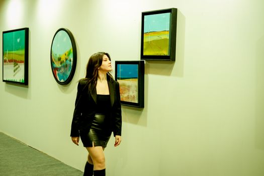 Woman in a leather skirt exploring a vibrant art gallery exhibition.
