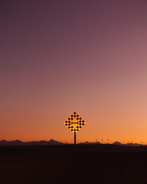 A Road Sign with Arrows Standing on the Background of Mountains at Sunset