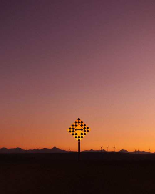 Free Silhouette of a directional road sign against a vibrant sunset with mountains in the background. Stock Photo