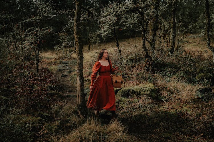 Woman In Red Medieval Dress Walking Through The Forest Carrying A Wicker Basket