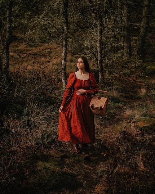 Model in Red Medieval Dress Carrying a Wicker Basket Through the Forest