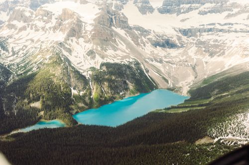 Free Stunning aerial view of a turquoise lake surrounded by lush forests and towering mountains. Stock Photo