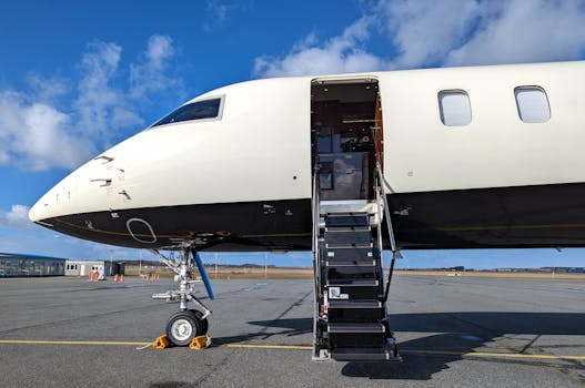 A private jet with an open door, parked on an airport ramp under a clear blue sky.
