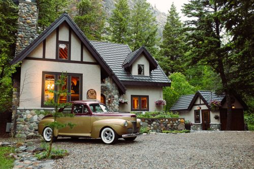 Free A classic vintage car parked in front of a picturesque cabin surrounded by lush forest trees. Stock Photo