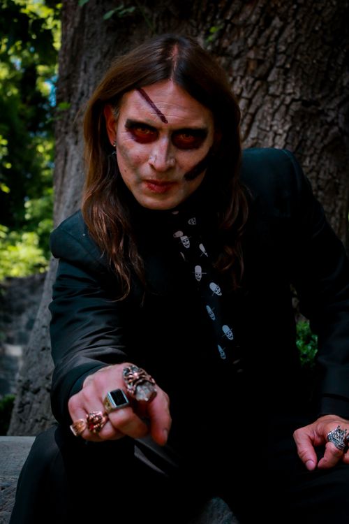 Free A man with dark makeup and gothic attire poses outdoors, showcasing elaborate rings and a mysterious expression. Stock Photo