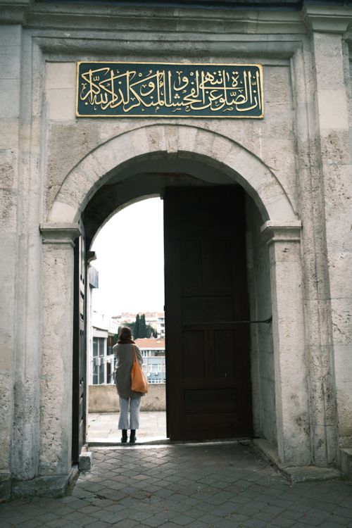 Free A woman stands at a historic stone archway with elegant non-Western script above. Stock Photo