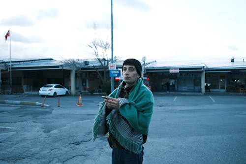 Young Man with a Blanket over His Shoulders Standing Outdoors 