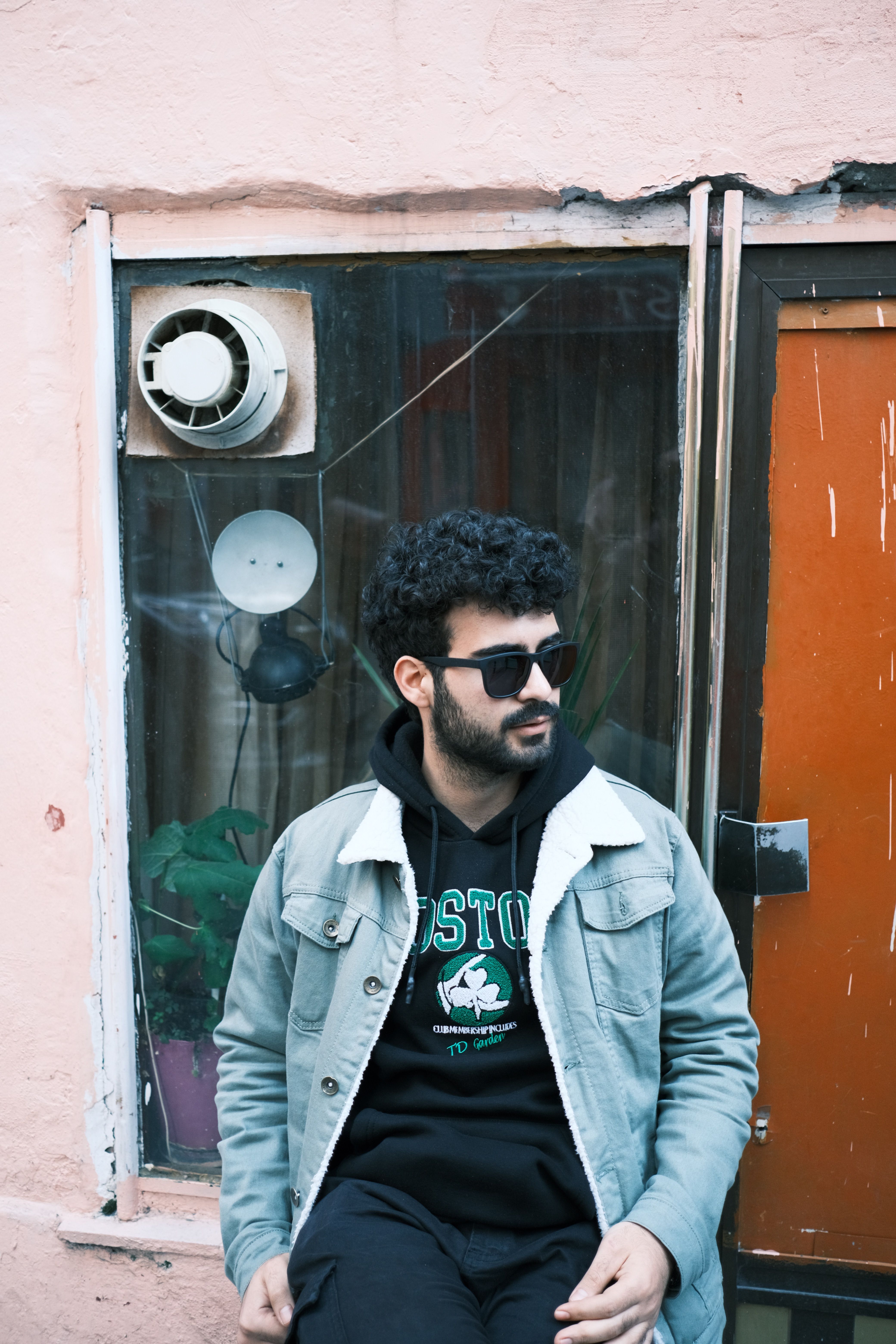 Young man with sunglasses and denim jacket sitting outside. Urban vibe.