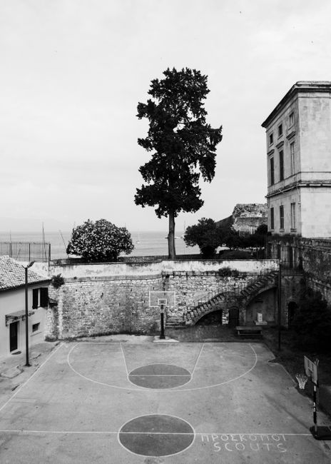 Aerial black and white photograph of a historic urban basketball court in Kerkyra, Greece, showcasing a tree and architecture.