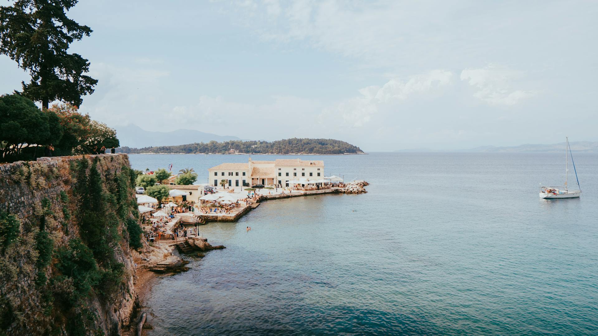 A picturesque view of the coastline in Kerkyra, Greece with a sailing boat and serene waters.