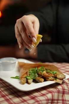 Close-up of lemon being squeezed over freshly made fried fish tacos on a white plate.