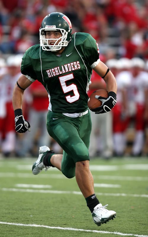 Free Man Wearing Green American Football Jersey Holding the Ball While Running on the Field Stock Photo