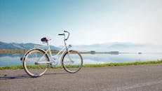 一辆老式自行车停在湖边的道路上，晴朗的天空下可以望见远处的山景