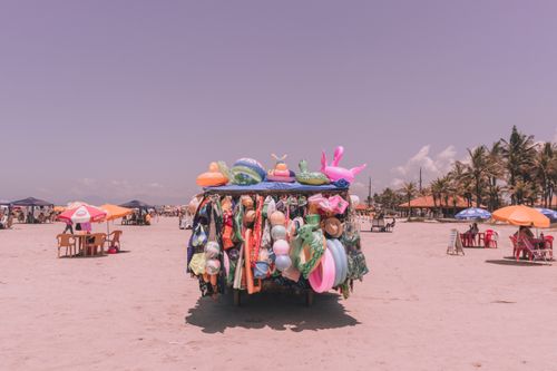 Free Colorful beach accessories shop on a sandy beach with palm trees and umbrellas. Stock Photo