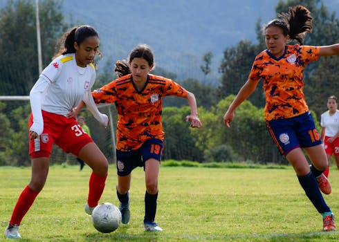 Teenage girls competing in a lively soccer match outdoors on a sunny day.