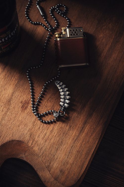 Free Close-up of a silver rattlesnake tail pendant and lighter on a wooden board. Stock Photo
