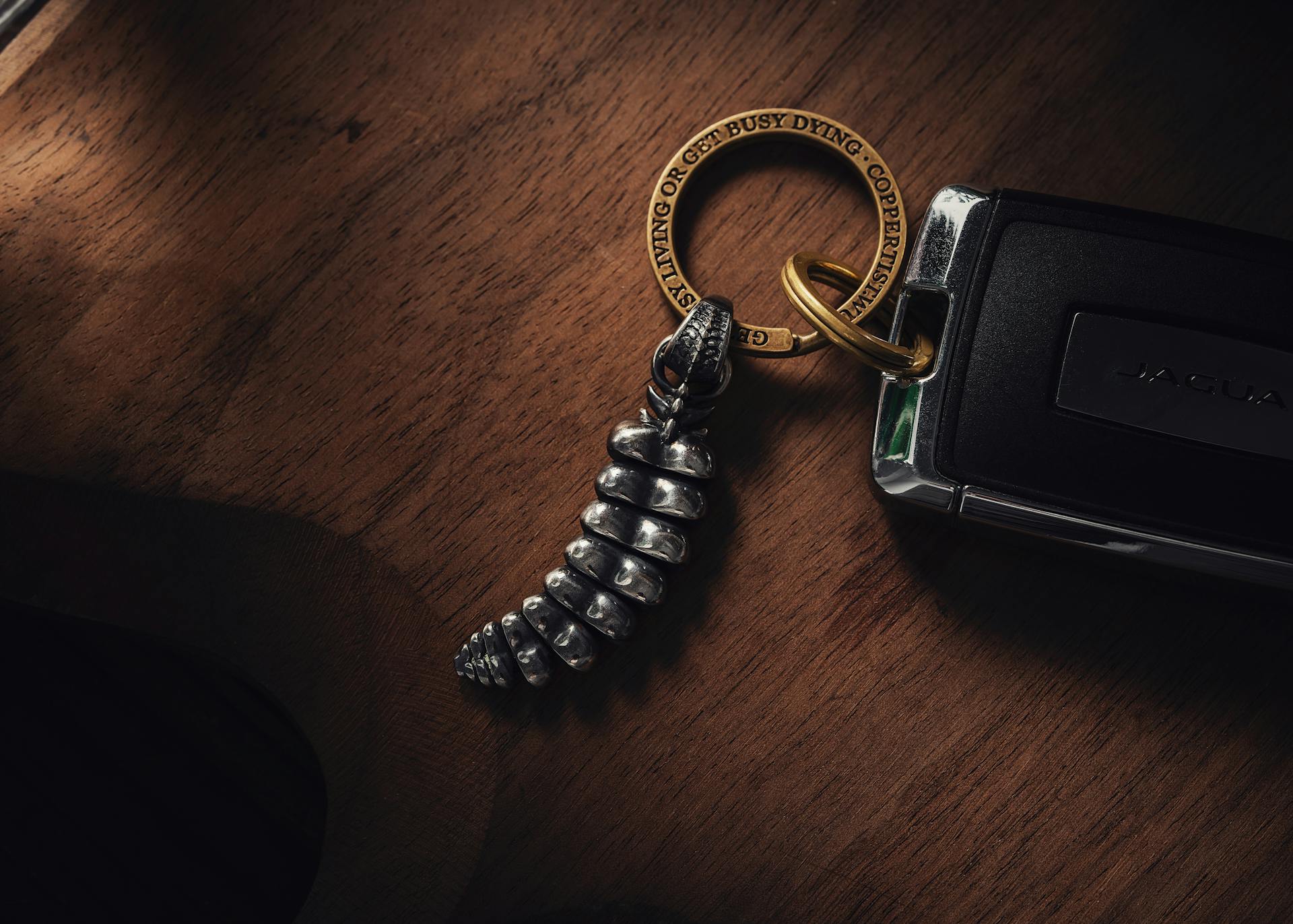 Close-up image of a silver rattlesnake tail keychain attached to a luxury car key over a wooden surface.