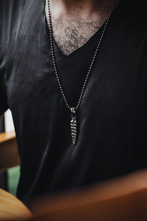 Free Close-up of a man wearing a silver necklace with a pendant, showcasing modern fashion accessories. Stock Photo