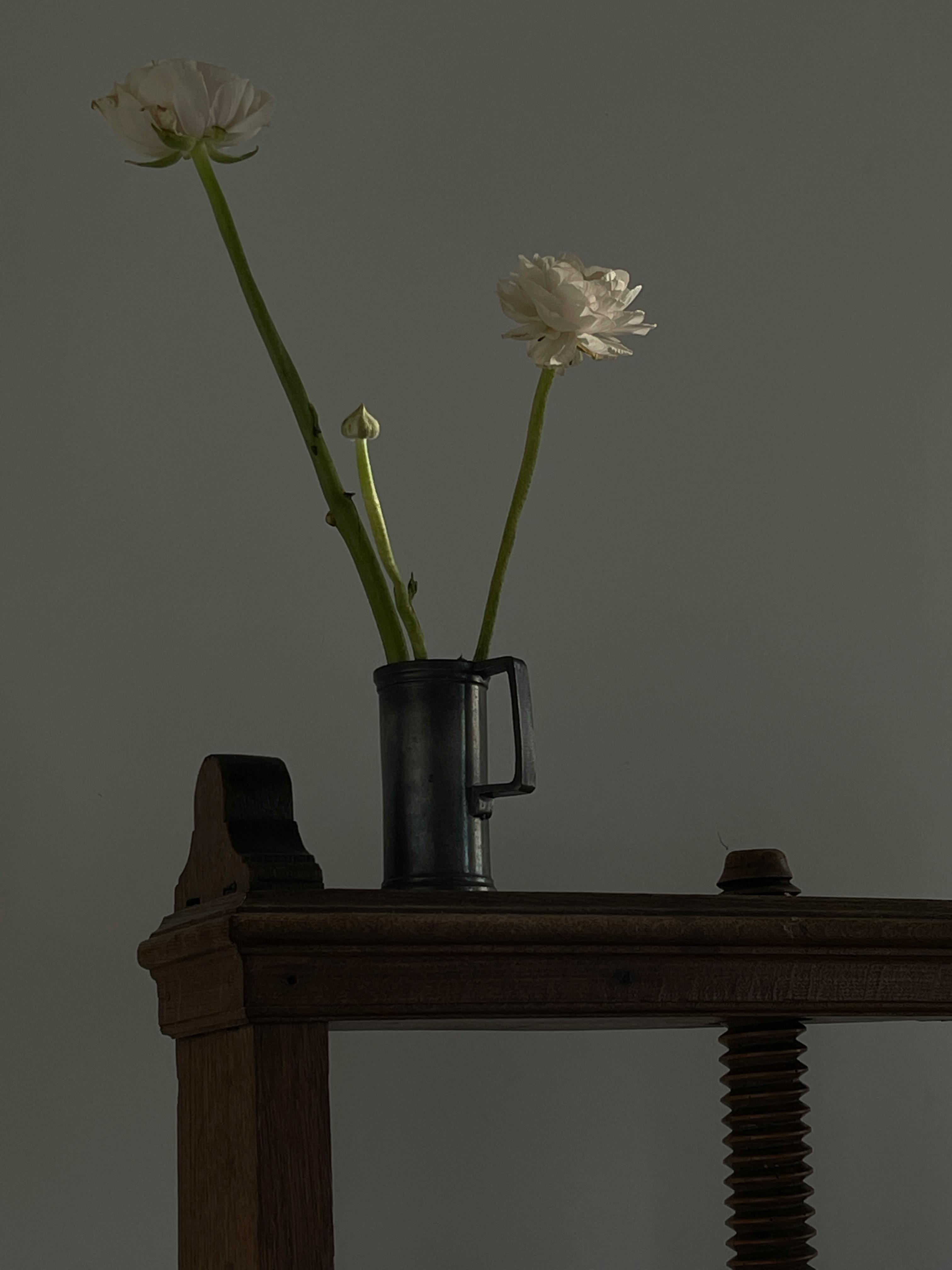 A simple and elegant floral display with white flowers in a dark metal vase on a wooden table.