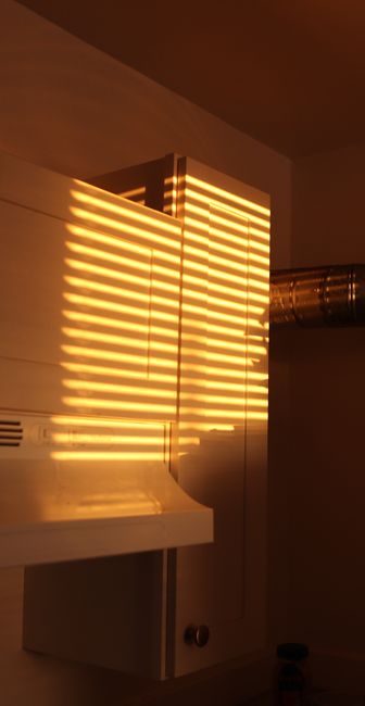 Fotomural Luz cálida del atardecer proyectando sombras a rayas en un armario de cocina, creando un ambiente acogedor.