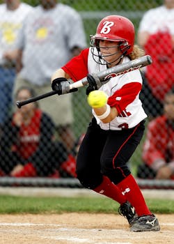 Focused female softball player in action swinging bat during outdoor game.
