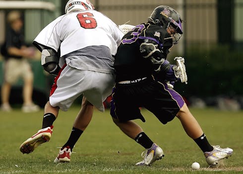 Competitive lacrosse match showing two players battling for control of the ball during an outdoor game.