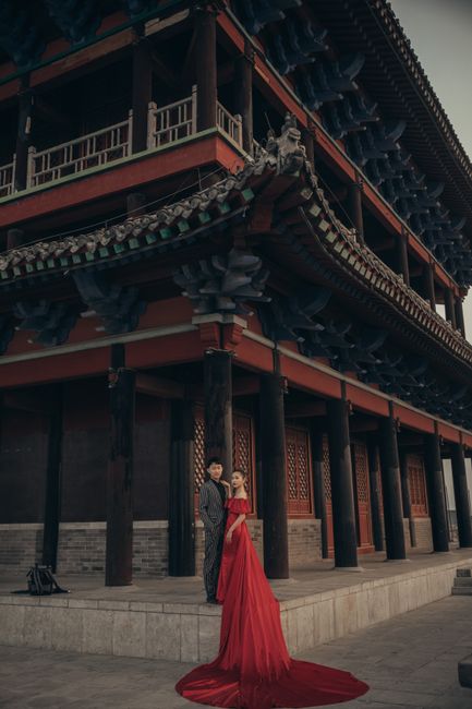 A couple poses elegantly in front of a traditional Chinese building, showcasing a mix of fashion and cultural heritage.