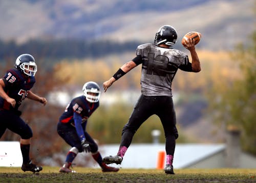 2 Football Player Running After Person Holding Football during Daytime in Shallow Focus Photography