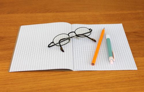 Free Open notebook with graph paper, eyeglasses, and pencils on a wooden table. Stock Photo