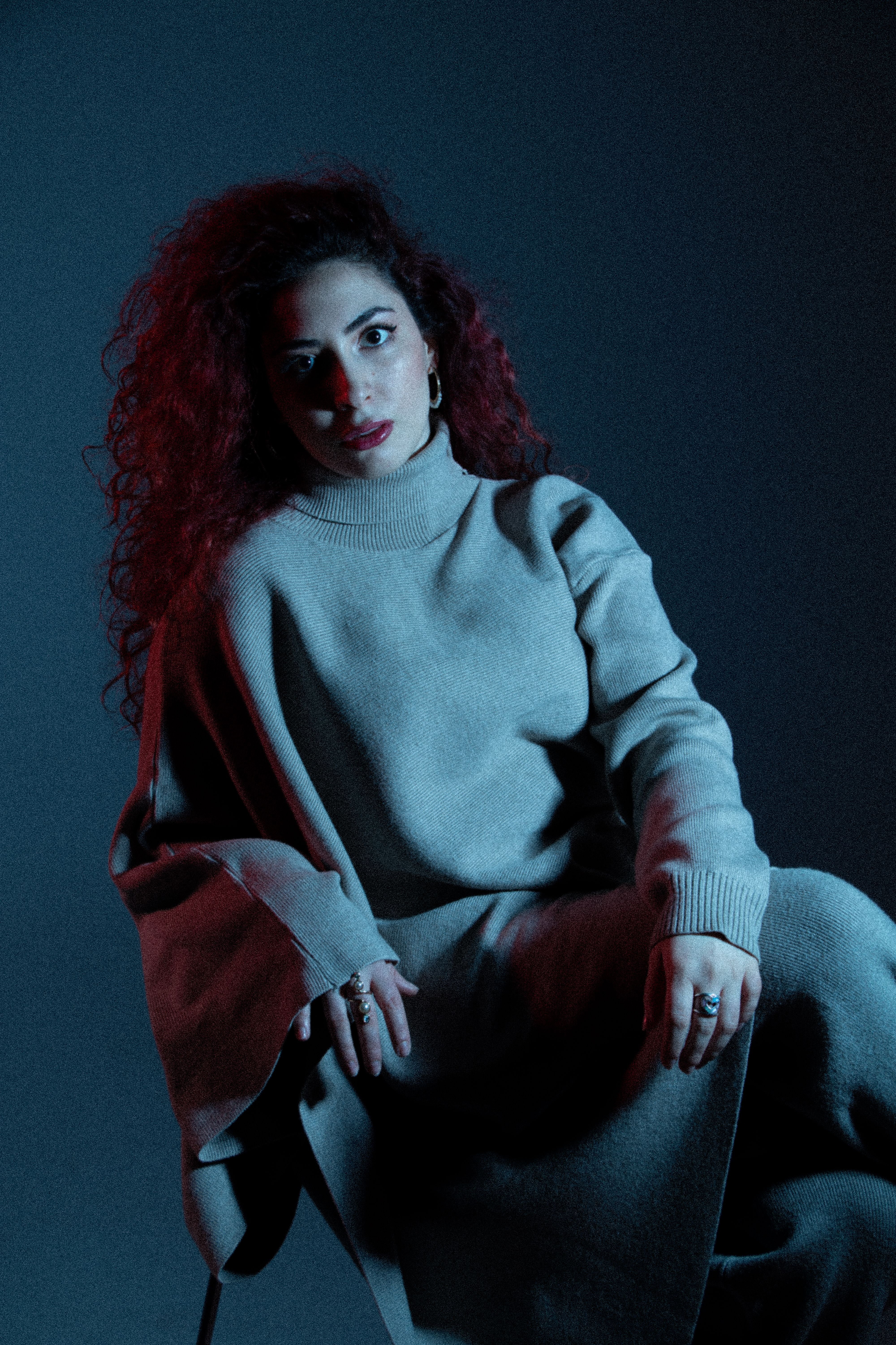 Dramatic studio portrait of a woman in a cozy sweater under blue and red lighting.