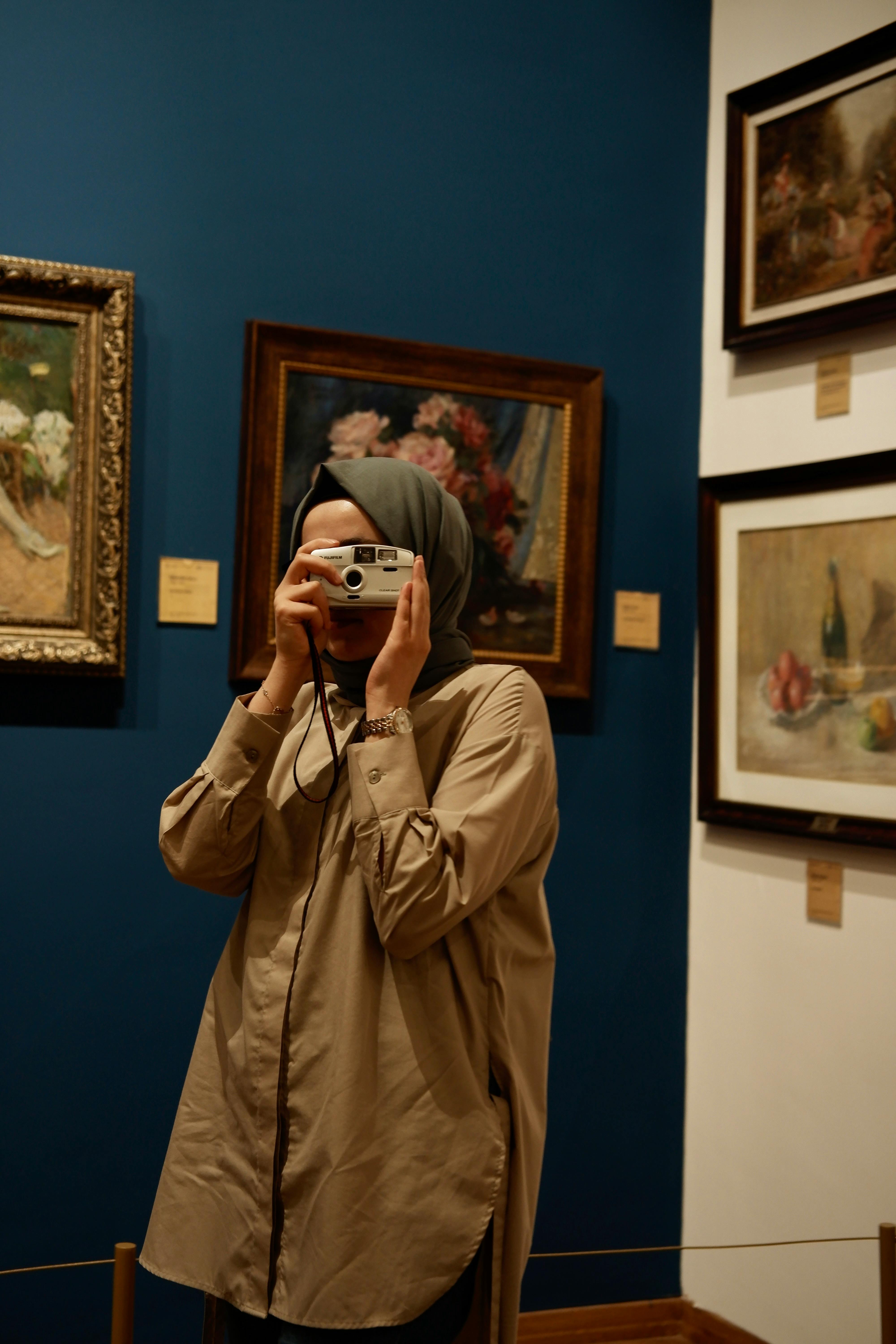 A woman wearing a headscarf takes a picture of art in a museum.