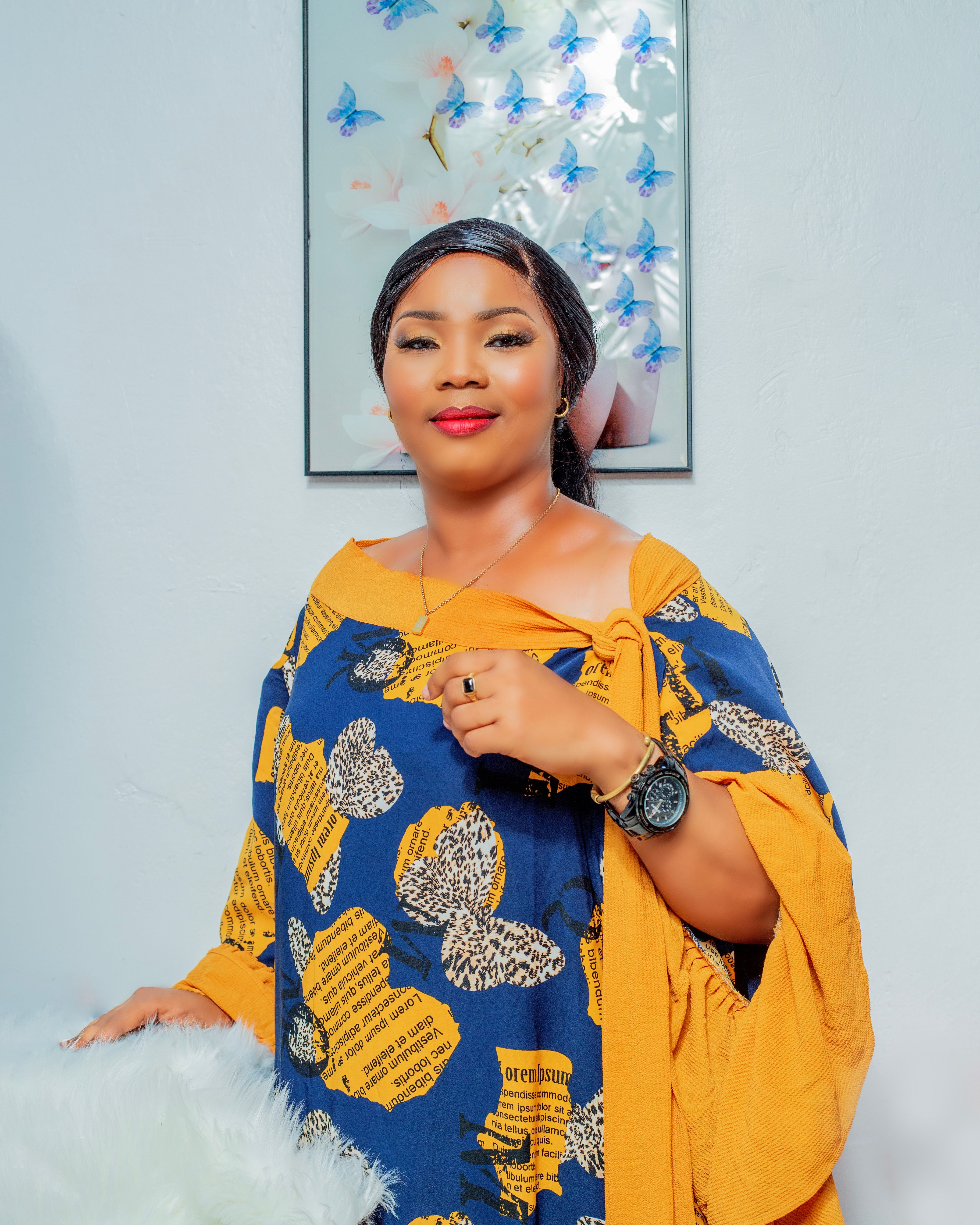 A woman in a patterned dress with butterflies, standing indoors, exuding elegance.