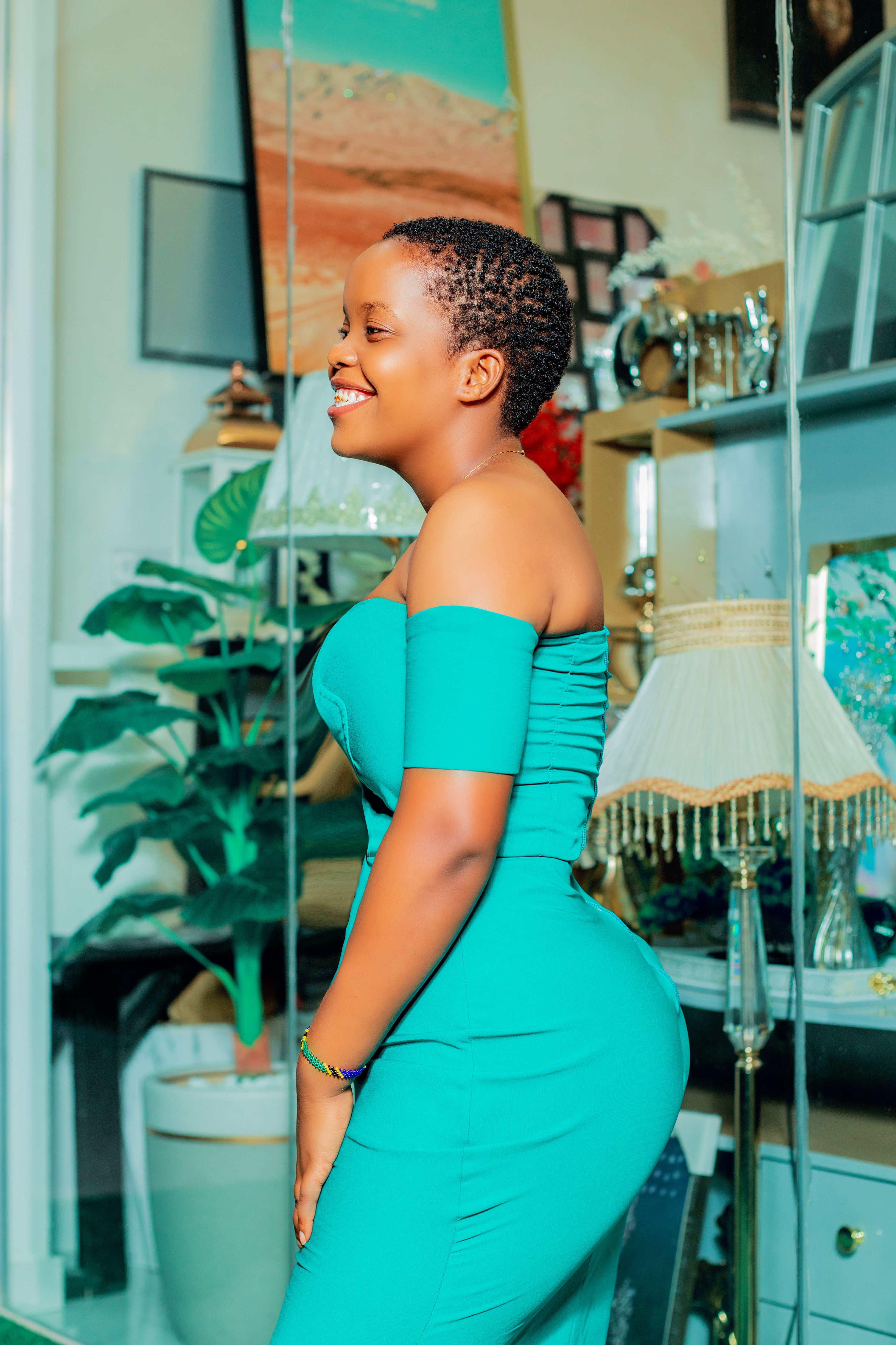 A woman with short black hair poses happily in a green dress, standing indoors.