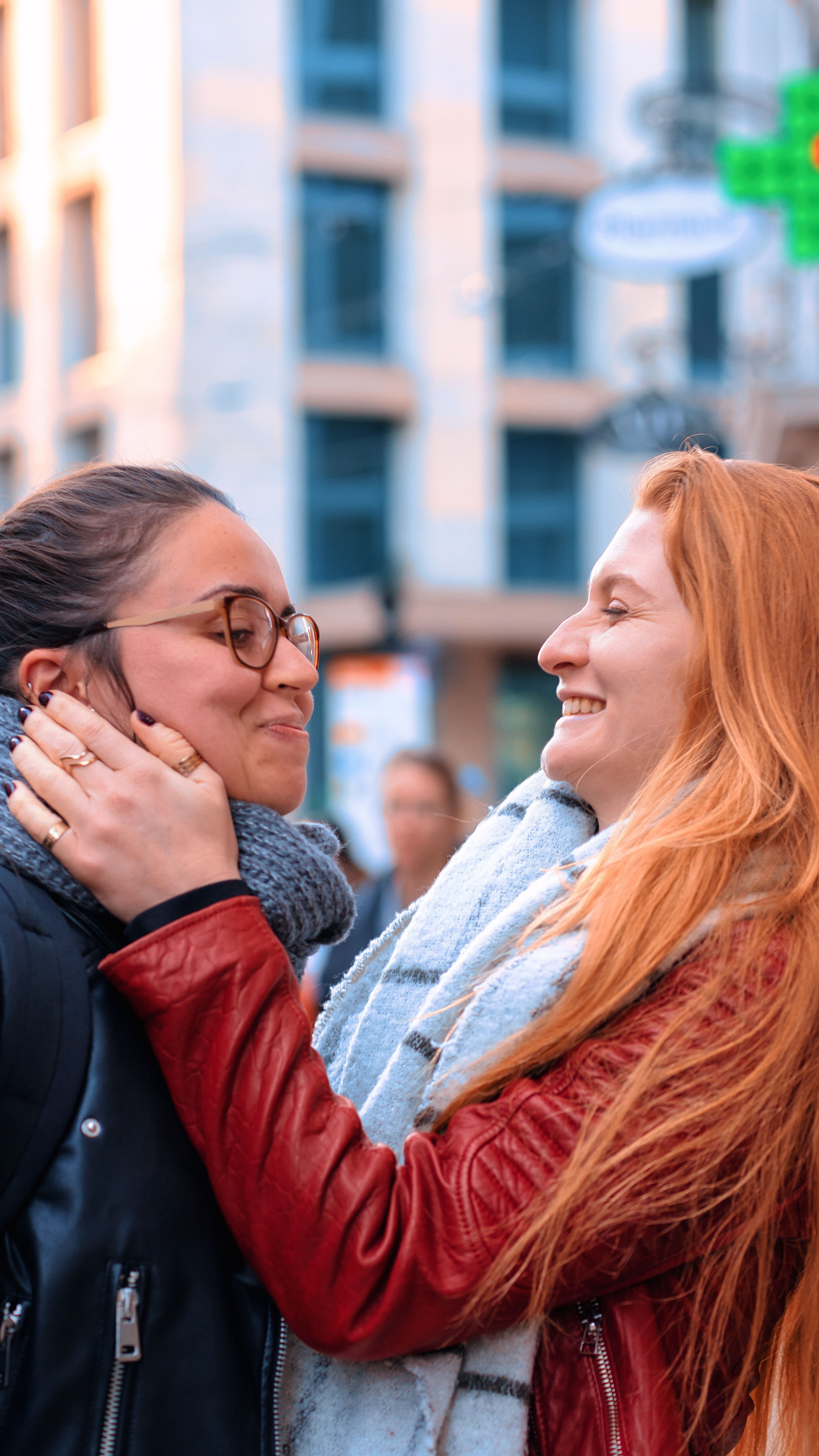 Two women embracing and smiling warmly against an urban backdrop, symbolizing love and happiness.