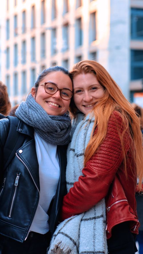 Free Two women smiling warmly in fashionable jackets and scarfs, enjoying an outdoor urban setting. Stock Photo