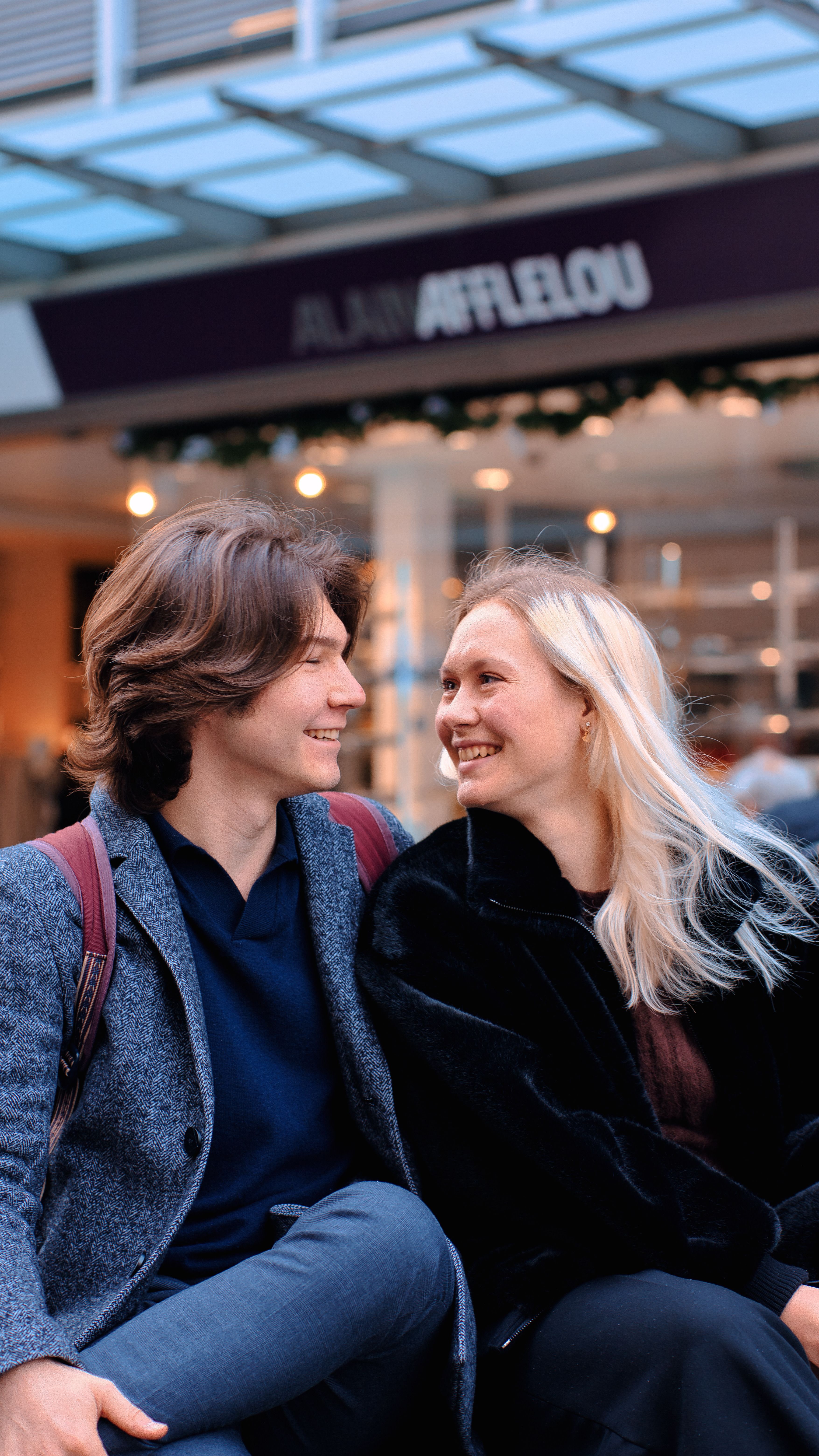 A cheerful young couple smiling at each other in a vibrant urban location, enjoying a moment together.
