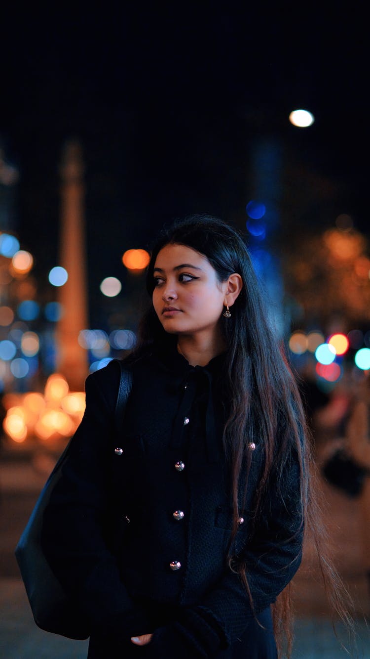 Young Woman In A Black Wool Coat Standing In A City Street At Night