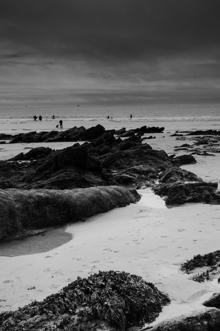 Black and white photo of a rocky seashore with ocean horizon and cloudy sky.