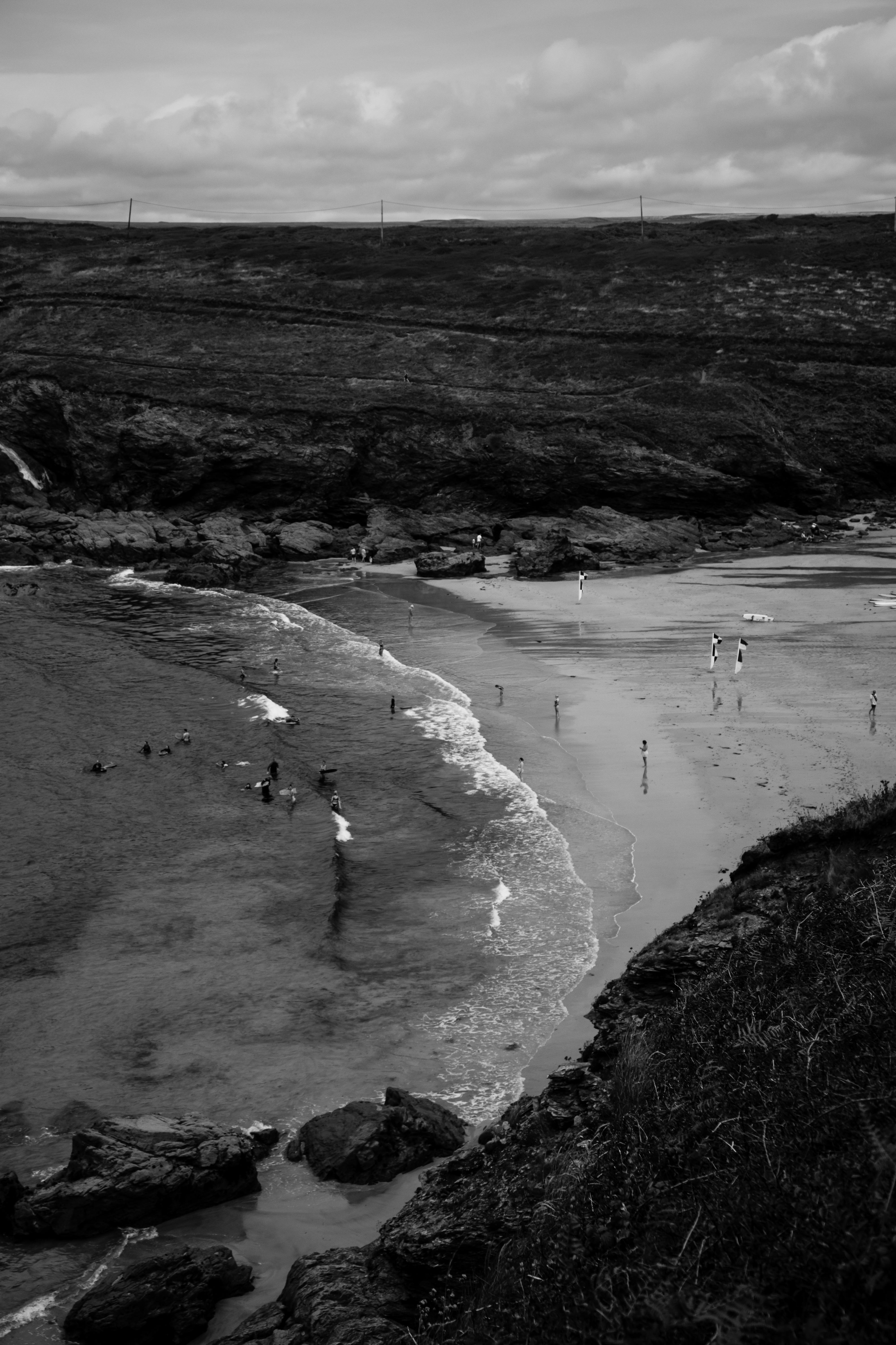 A dramatic black and white aerial view of a serene beach with gentle waves and scattered beachgoers.