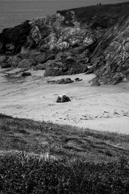 Monochrome image of a secluded tent on a sandy beach surrounded by rocky cliffs.